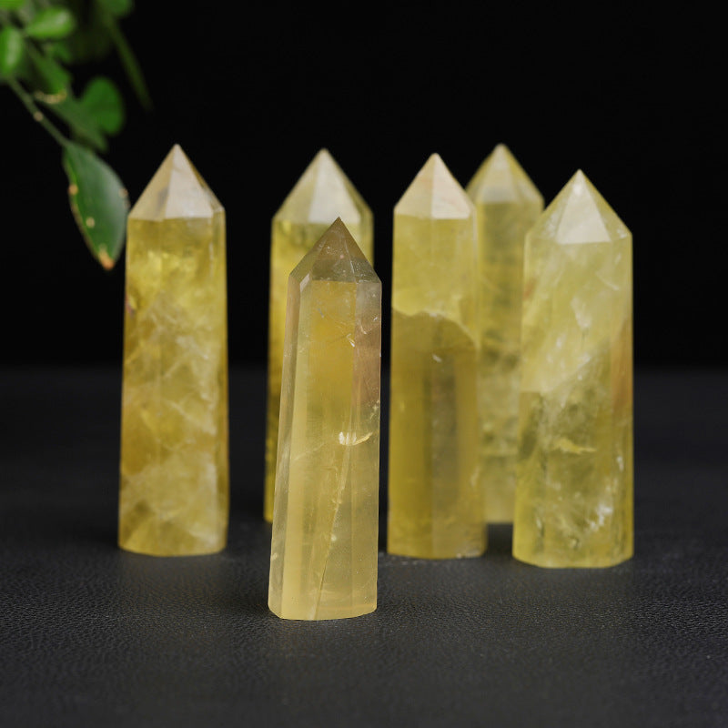 Citrine crystal tower group with one pale yellow point in front and five taller points behind, each showing six polished sides, cloudy inner marks, and a faceted top, under lights.