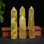 Citrine crystal tower display with five yellow polished points in two rows, three on a wood stand and two in front, against a black backdrop with green leaves nearby, under lights.