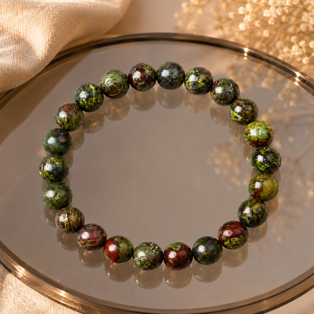 Dragon blood stone bracelet on gold-rimmed mirror tray with green leaves, natural healing stone stretch bracelet