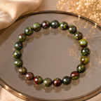 Dragon blood stone bracelet on gold-rimmed mirror tray with green leaves, natural healing stone stretch bracelet
