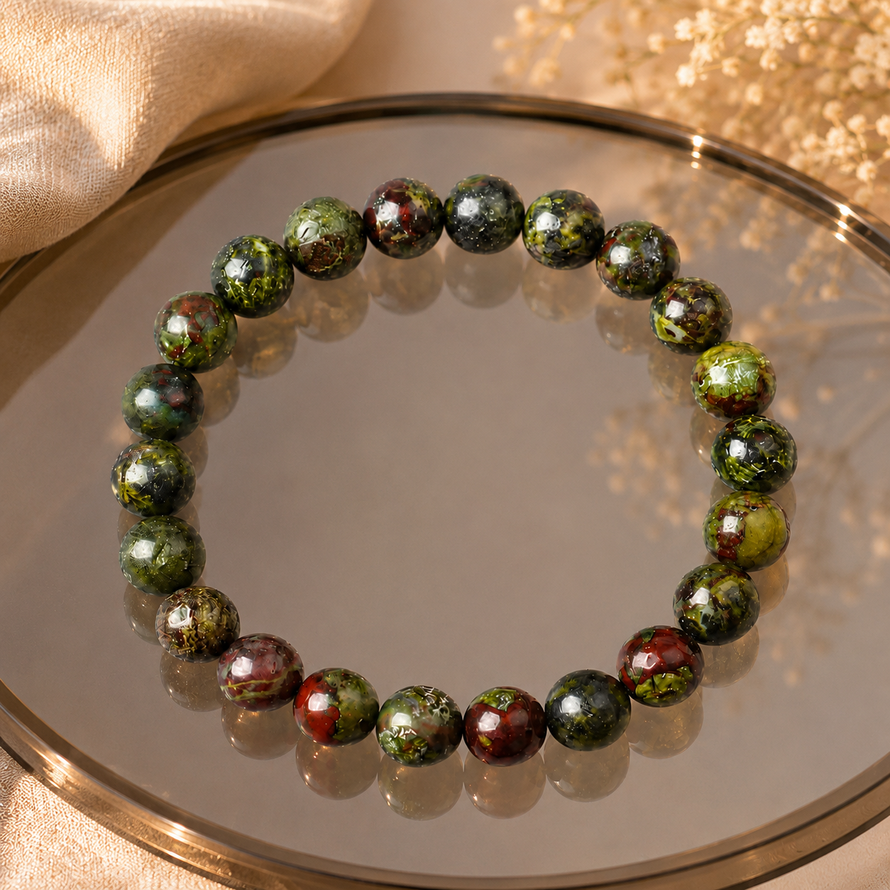 Dragon blood stone bracelet on gold-rimmed mirror tray with green leaves, natural healing stone stretch bracelet