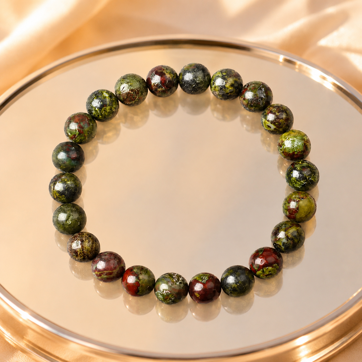 Dragon blood stone bracelet on gold mirror tray with warm satin backdrop, premium green red gemstone jewelry