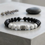 Gemini bracelet on gray stone with black onyx, white howlite beads, silver charm, and lavender for daily calm focus