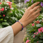 Hand wearing a colorful beaded gemini bracelet with flowers in the background