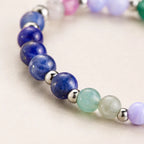 Close-up of a gemini zodiac bracelet with blue, green, and silver beads on a light background