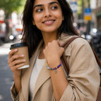 Woman holding a coffee cup and smiling on a city street wearing a gemini zodiac bracelet