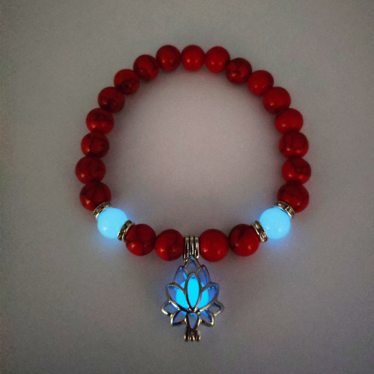 Glow in the dark lotus bracelet red stone beads with a blue glow view, with 8 mm real-stone beads, elastic fit, a silver-color lotus, and light-charged accents for glow after dark.