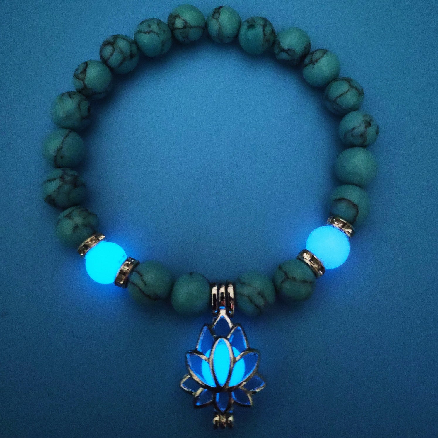 Glow in the dark lotus bracelet blue-green beads with a blue glow view, with 8 mm real-stone beads, elastic fit, a silver-color lotus, and light-charged accents for low-light wear.