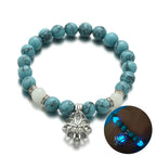 Glow in the dark lotus bracelet blue-green stone hero view and glow inset, with 8 mm real-stone beads, elastic fit, a silver-color lotus, and light-charged accents for daily style.