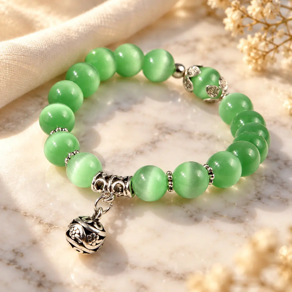 Green catseye bracelet featuring glossy green beads and ornate silver charm, styled in warm light for a graceful jewelry look.