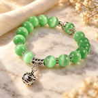 Green catseye bracelet featuring glossy green beads and ornate silver charm, styled in warm light for a graceful jewelry look.