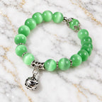 Green catseye bracelet featuring luminous green beads and detailed silver floral charm, displayed on white marble for timeless style.