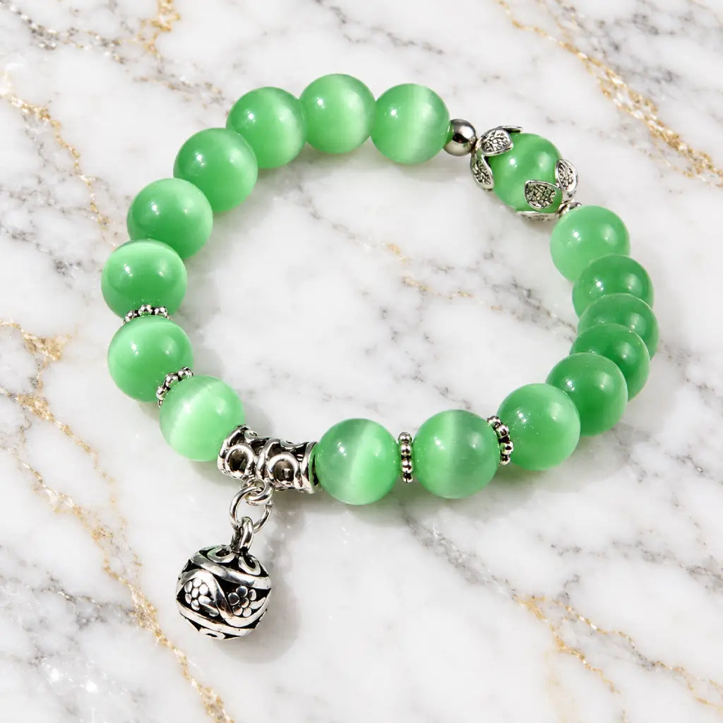 Green catseye bracelet featuring luminous green beads and detailed silver floral charm, displayed on white marble for timeless style.