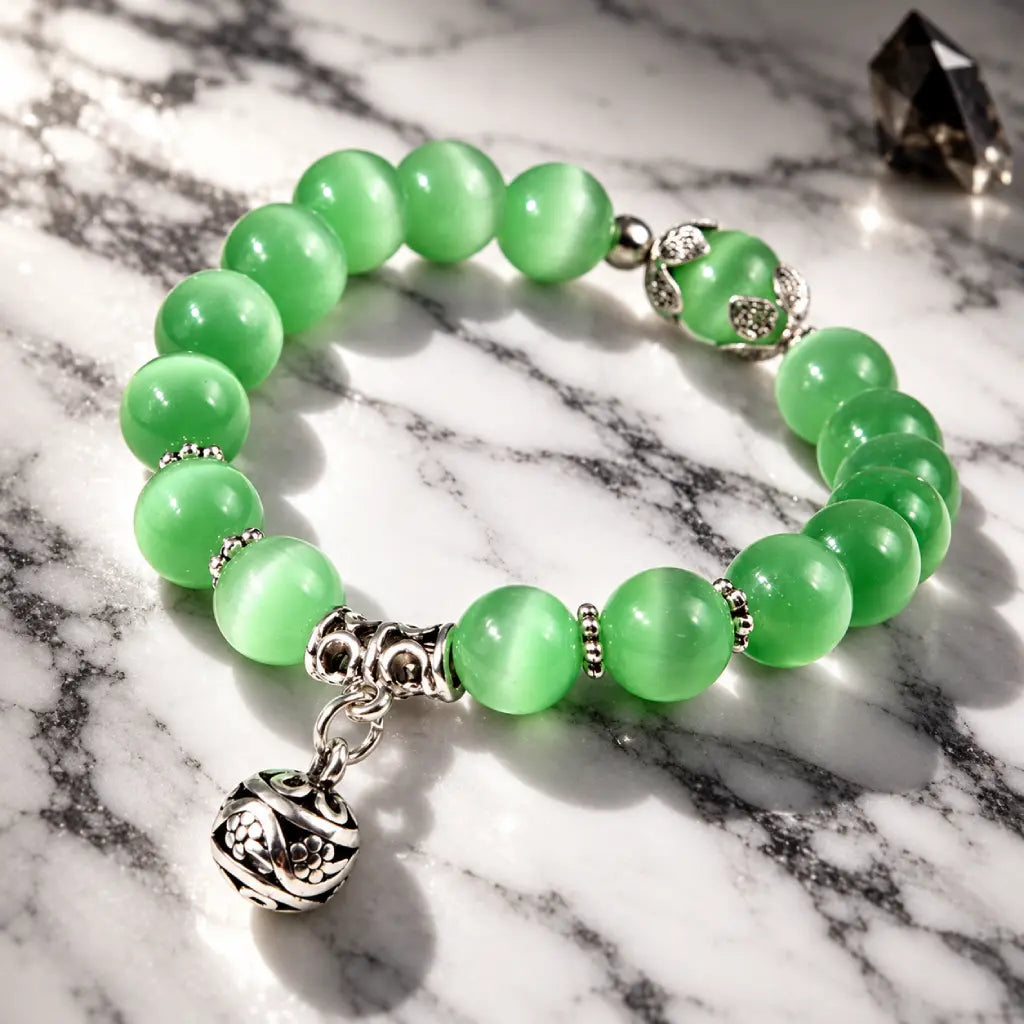 Green catseye bracelet with luminous round beads, silver spacers and floral charm, displayed on marble for elegant style.