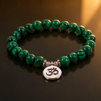 Green tigereye gemstone bracelet displayed on dark reflective surface with polished Om charm details