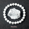Howlite beads arranged in a circle with a howlite stone in the center on a dark fabric background.