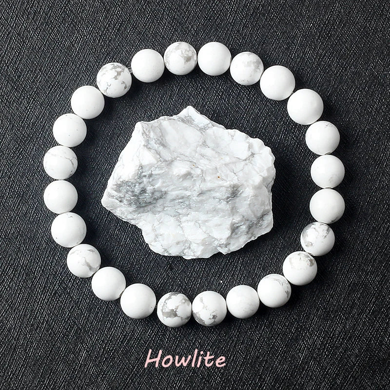 Howlite beads arranged in a circle with a howlite stone in the center on a dark fabric background.