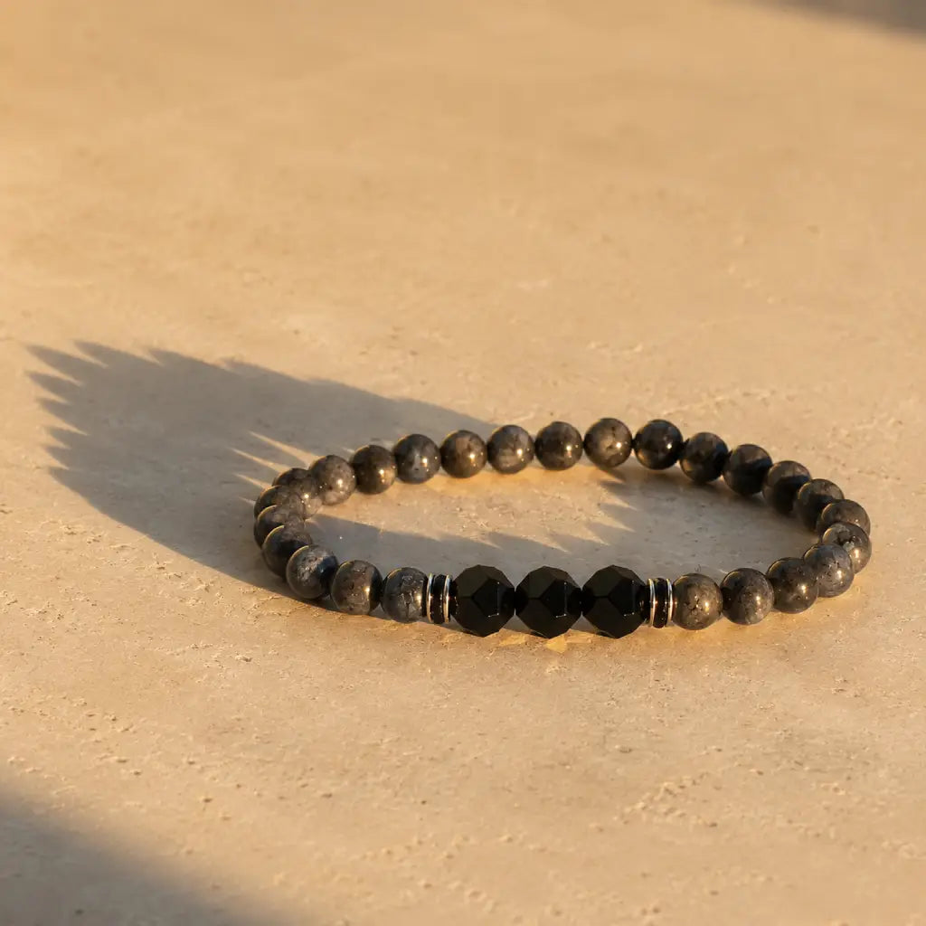 Labradorite and Obsidian bracelet with faceted black stones on warm marble surface for elegant energy style.