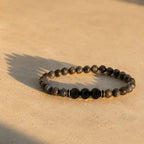 Labradorite and Obsidian bracelet with faceted black stones on warm marble surface for elegant energy style.