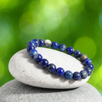 Lapis lazuli bracelet resting on stacked stones with green bokeh, polished healing crystal jewelry for calm style