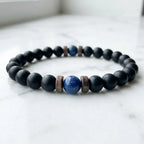 Lapis lazuli center stone black onyx beaded bracelet resting on white marble, minimalist product photography natural crystal healing bracelet