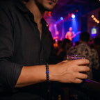 Lapis Lazuli onyx bracelet worn by a man holding a drink at a nightclub, showcasing matte black onyx beads with a blue lapis lazuli centerpiece.