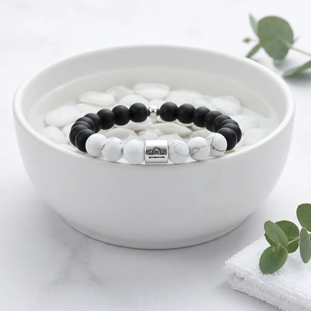 Black and white beaded bracelet in a white bowl with eucalyptus leaves on a light background
