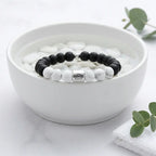 Black and white beaded bracelet in a white bowl with eucalyptus leaves on a light background
