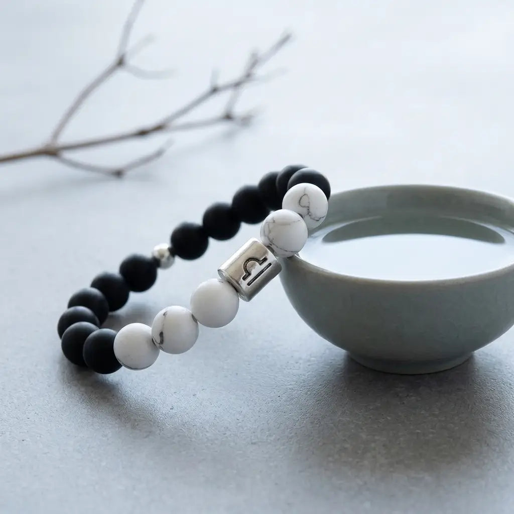 Black and white beaded bracelet with a silver charm on a light gray surface with a ceramic cup.