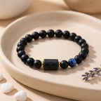 Libra zodiac bracelet with matte black beads, blue accent stone, and engraved center bead on a ceramic tray.