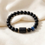 Libra zodiac bracelet with matte black beads, blue accent stone, and engraved center bead on soft cream fabric.