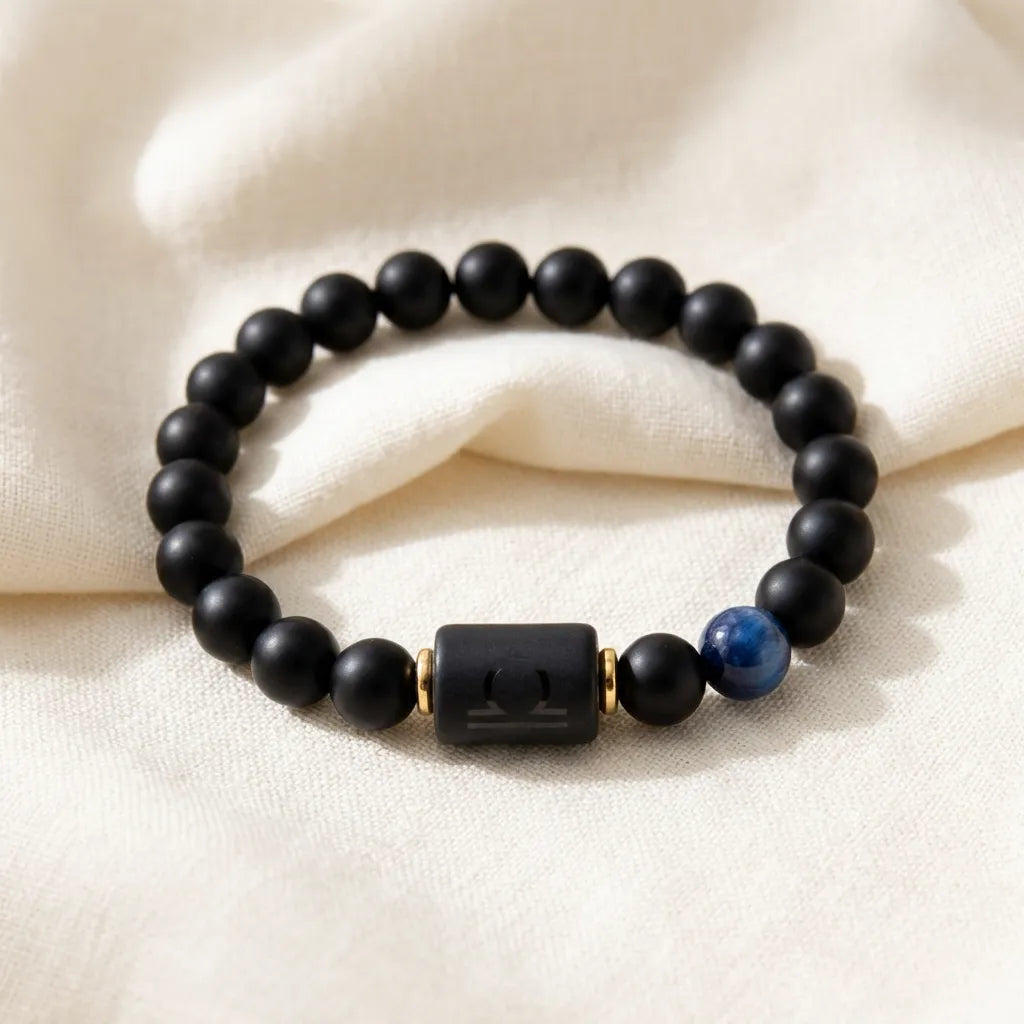 Libra zodiac bracelet with matte black beads, blue accent stone, and engraved center bead on soft cream fabric.