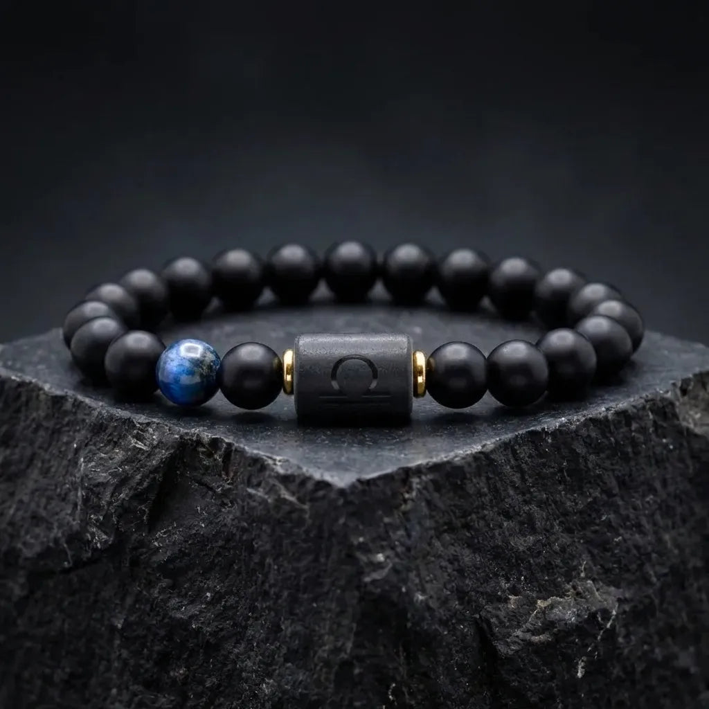 Libra zodiac bracelet with matte black beads, blue accent stone, and engraved center bead on black marble slab.