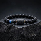 Libra zodiac bracelet with matte black beads, blue accent stone, and engraved center bead on black marble slab.