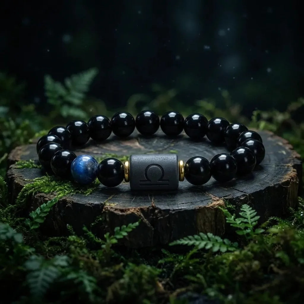 Libra zodiac bracelet with glossy black beads, blue accent stone, and engraved center bead on a forest stump.