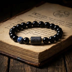 Libra zodiac bracelet with glossy black beads, blue accent stone, and engraved center bead on an old book.