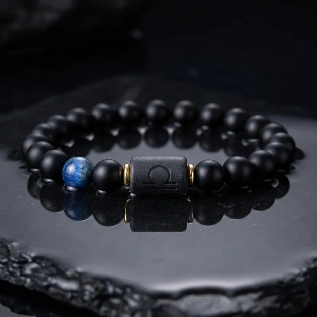 Libra zodiac bracelet with matte black beads, blue accent stone, and engraved center bead on glossy black surface.