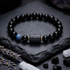 Libra zodiac bracelet with glossy black beads, blue accent stone, and engraved center bead on slate with crystals.