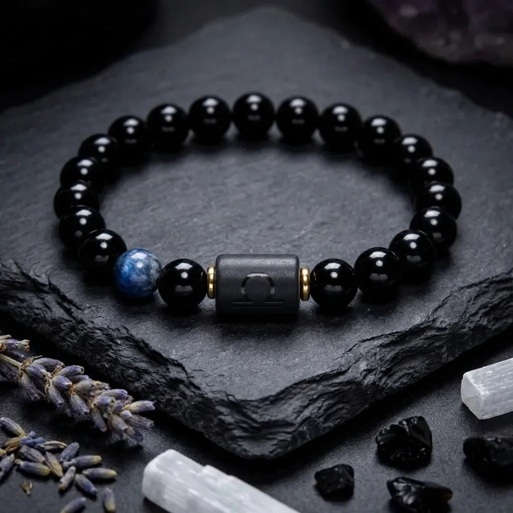Libra zodiac bracelet with glossy black beads, blue accent stone, and engraved center bead on slate with crystals.