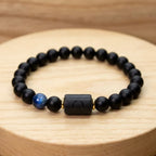 Libra zodiac bracelet with matte black beads, blue accent stone, and engraved center bead on a wooden surface.