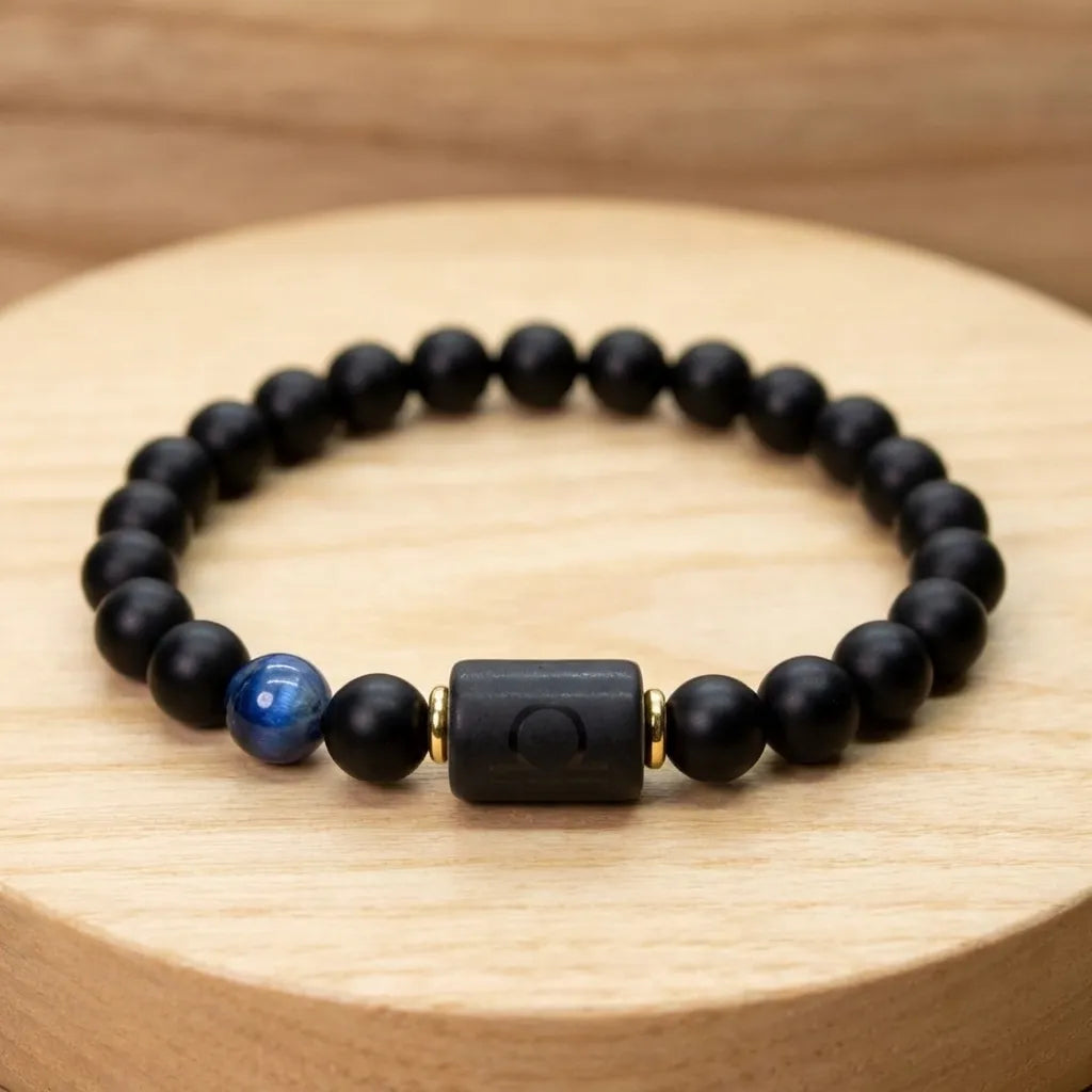 Libra zodiac bracelet with matte black beads, blue accent stone, and engraved center bead on a wooden surface.