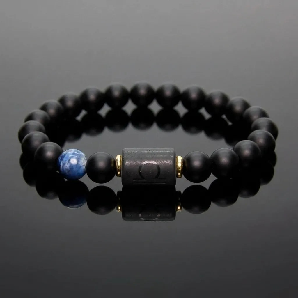 Libra zodiac bracelet with glossy black beads, blue accent stone, and engraved center bead on reflective surface.