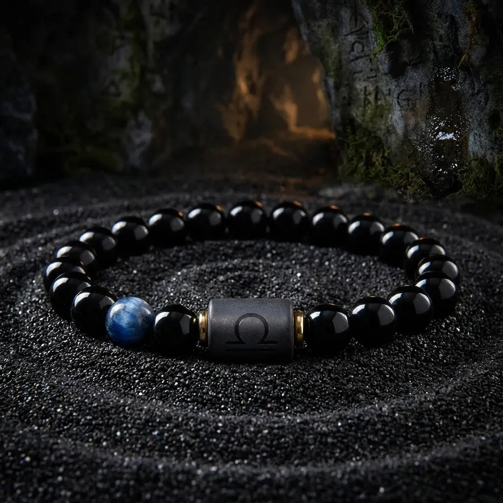 Libra zodiac bracelet with glossy black beads, blue accent stone, and engraved center bead on black sand.