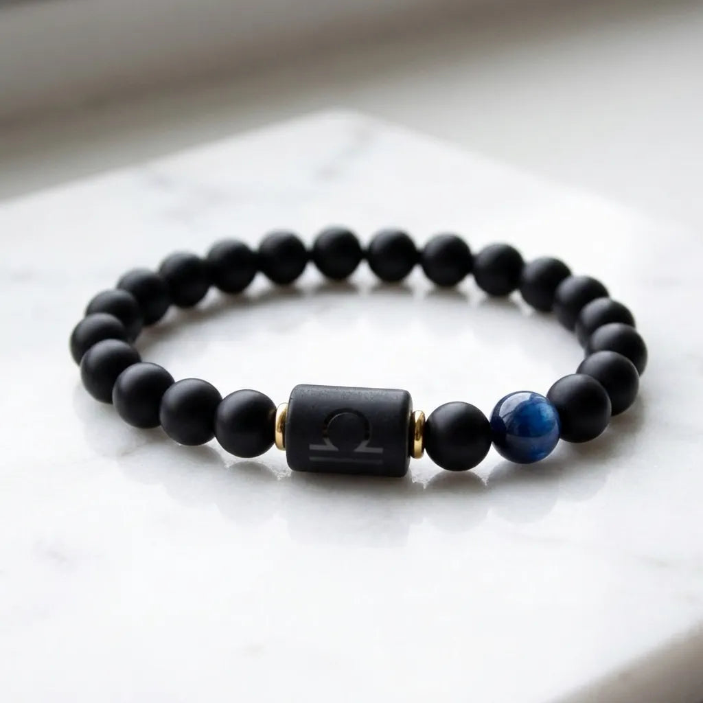 Libra zodiac bracelet with matte black beads, blue accent stone, and engraved center bead on white marble.