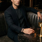 Libra zodiac bracelet worn by a man in a dark blazer, seated at a marble table in a lounge setting.