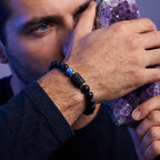 Libra zodiac bracelet worn on a man's wrist holding a purple crystal, featuring black beads and blue accent stone.