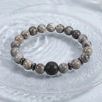 map jasper bracelet on frosted glass plate with gray beads and carved black charm for serene crystal style gift