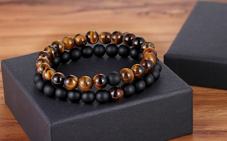 Matching bead bracelets for couples arranged as two coordinated glass-bead strands, pairing amber-brown striped round beads with matte black round beads on a black display box now.