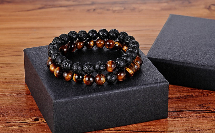 Matching bead bracelets for couples shown as two coordinated glass-bead strands, pairing black speckled round beads with amber-brown striped round beads on a black gift box nearby.