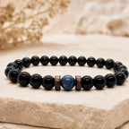 Obsidian lapis lazuli bracelet with polished black obsidian beads, natural blue lapis lazuli centerpiece, and wood spacers on a stone display.